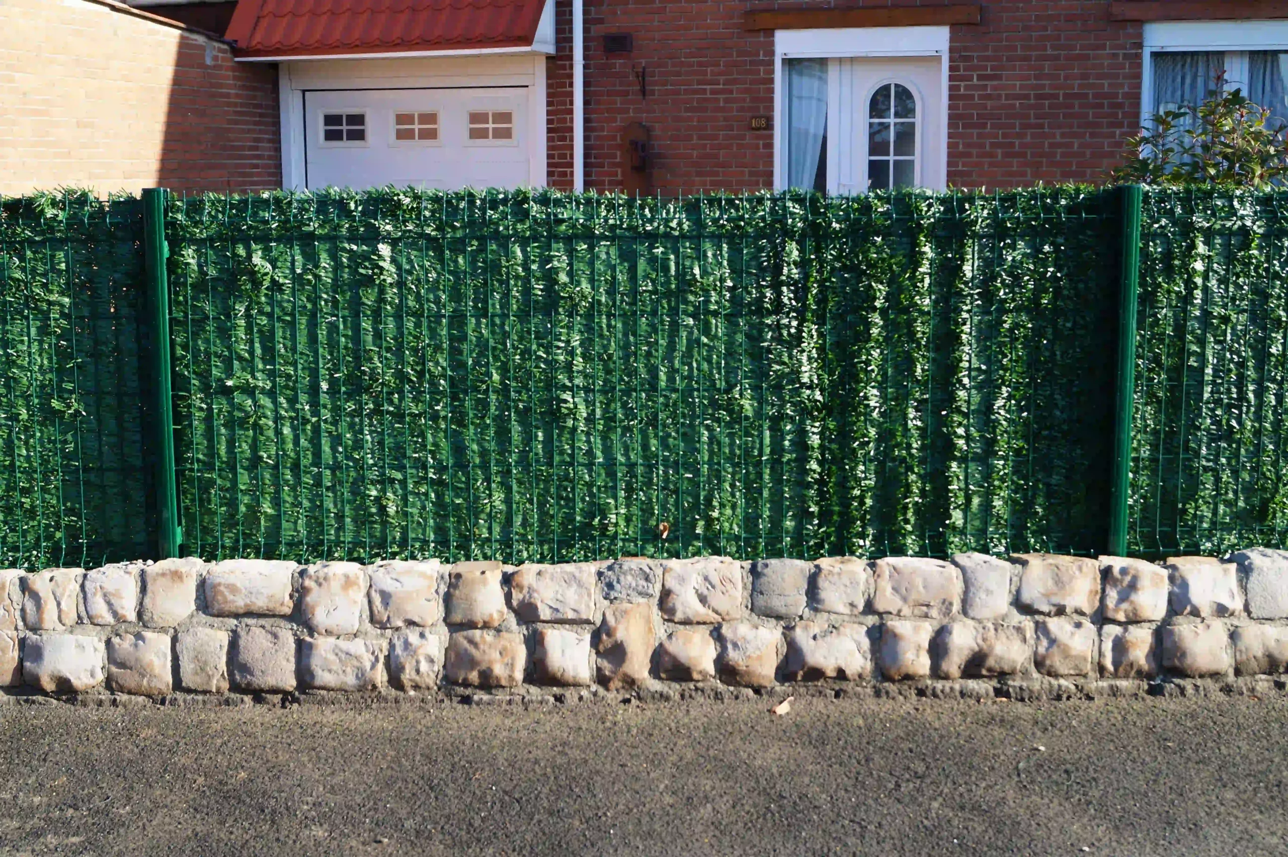Haie artificielle verte sur muret en pierre